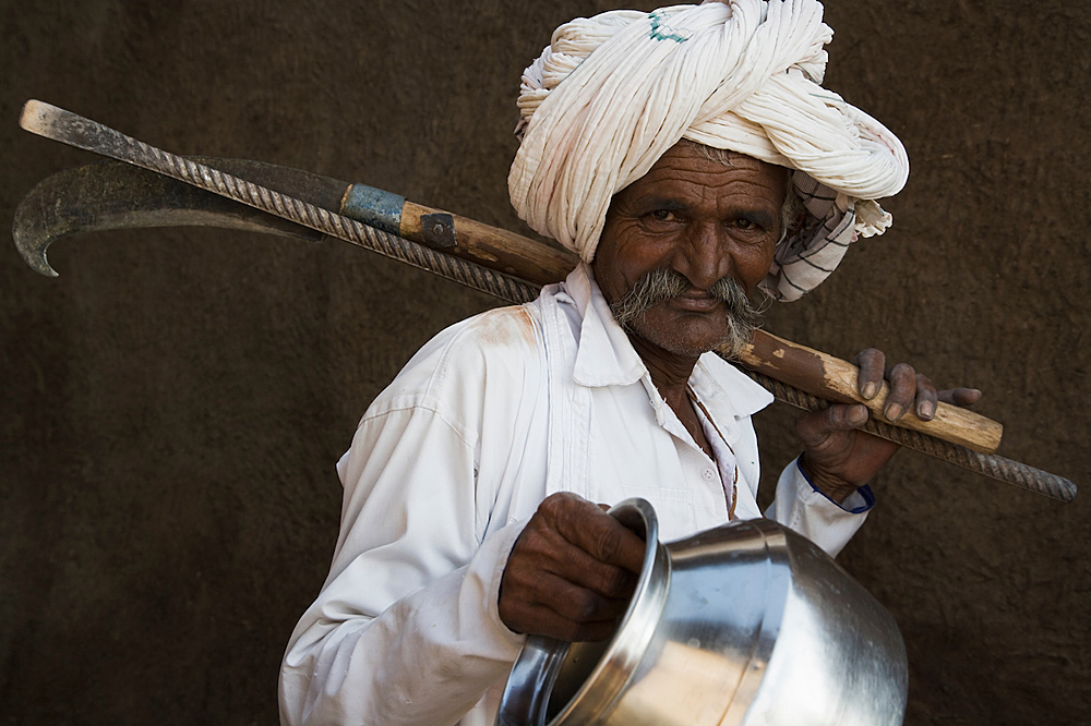 Old Gujarat man carrying tools and water jug